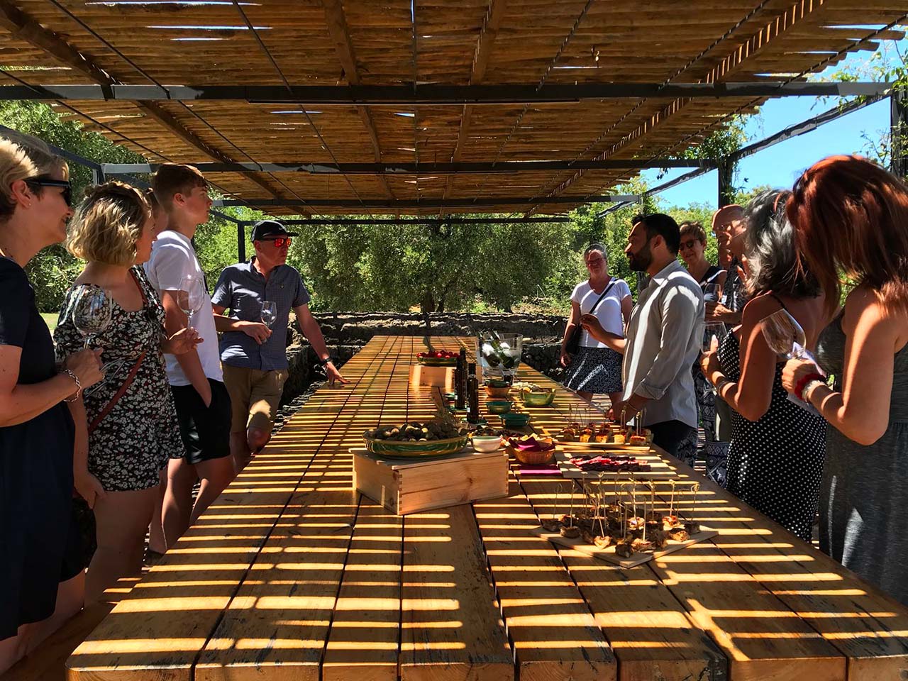 wine tasting at Planeta Sciaranuova, people around a long outdoor table covered by a pergola