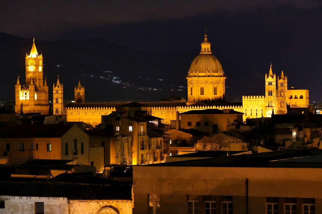 view of the roofs of Palermo at night, with the Cathedral in the background
